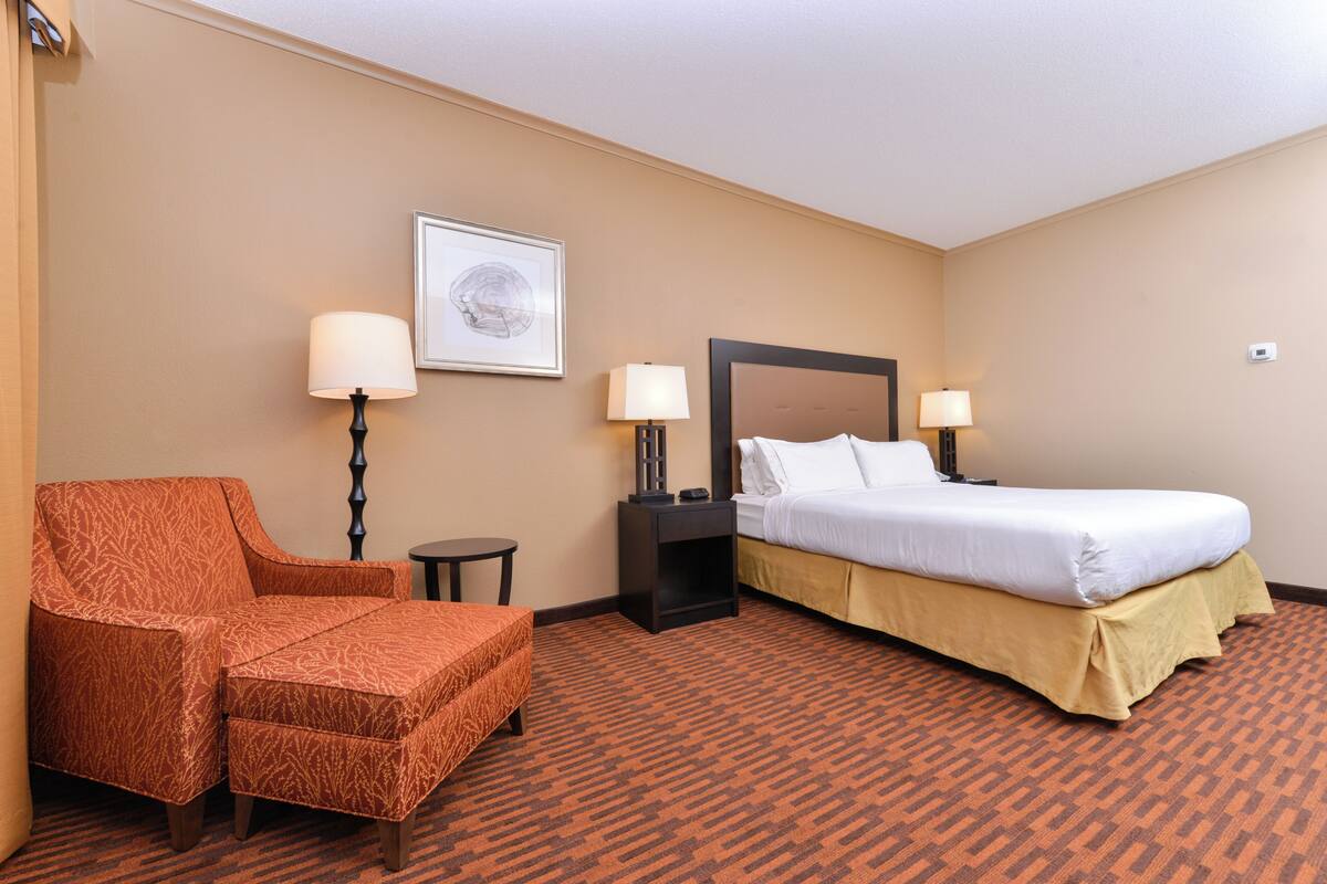 A hotel room with a bed, a chair, two nightstands with lamps, and a framed picture on the wall.