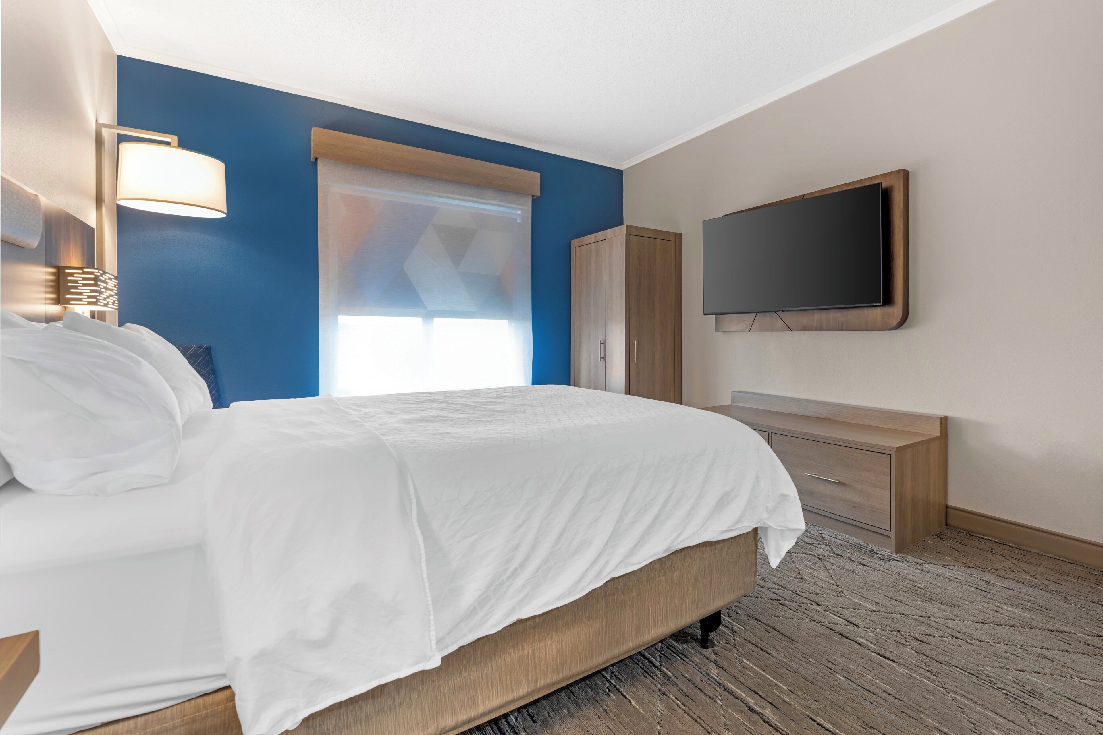 A hotel room with a bed, a TV, a wardrobe, and a window with blinds.