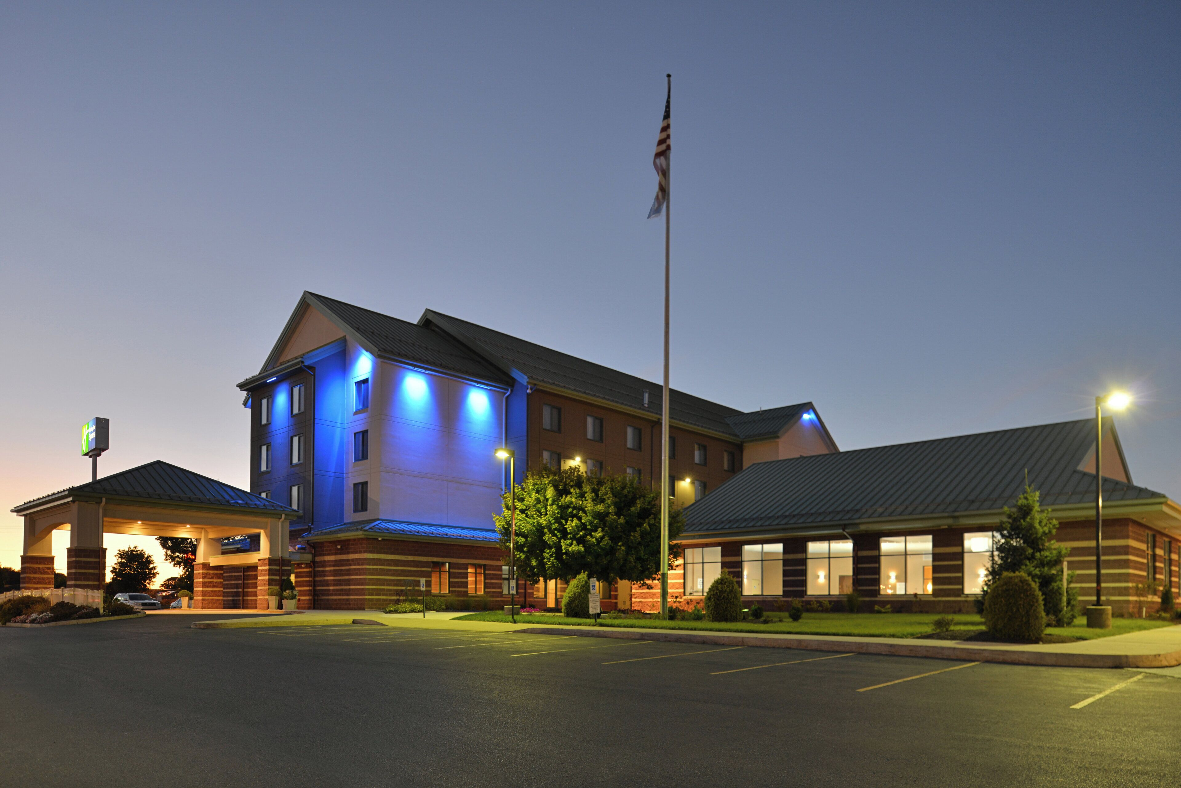 A hotel with a prominent building illuminated in blue, a flagpole with the American flag, and a parking lot.