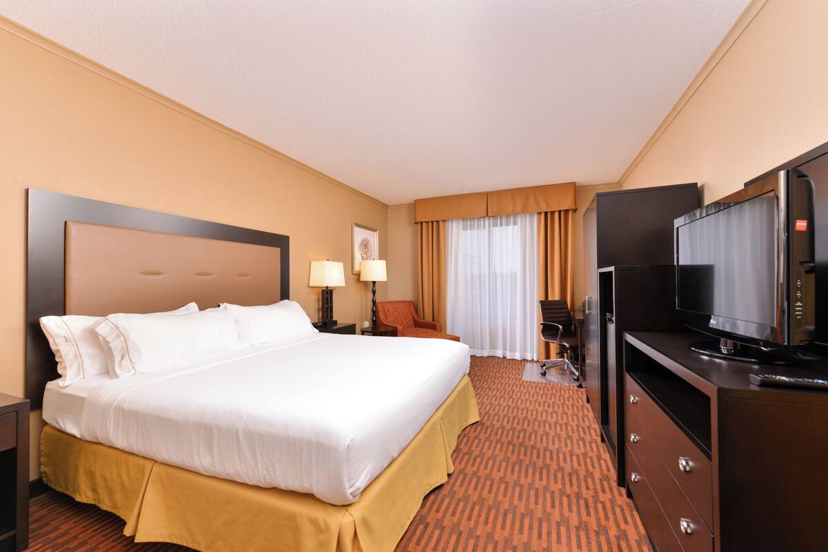 A hotel room with a large bed, a television, a desk, and a chair.
