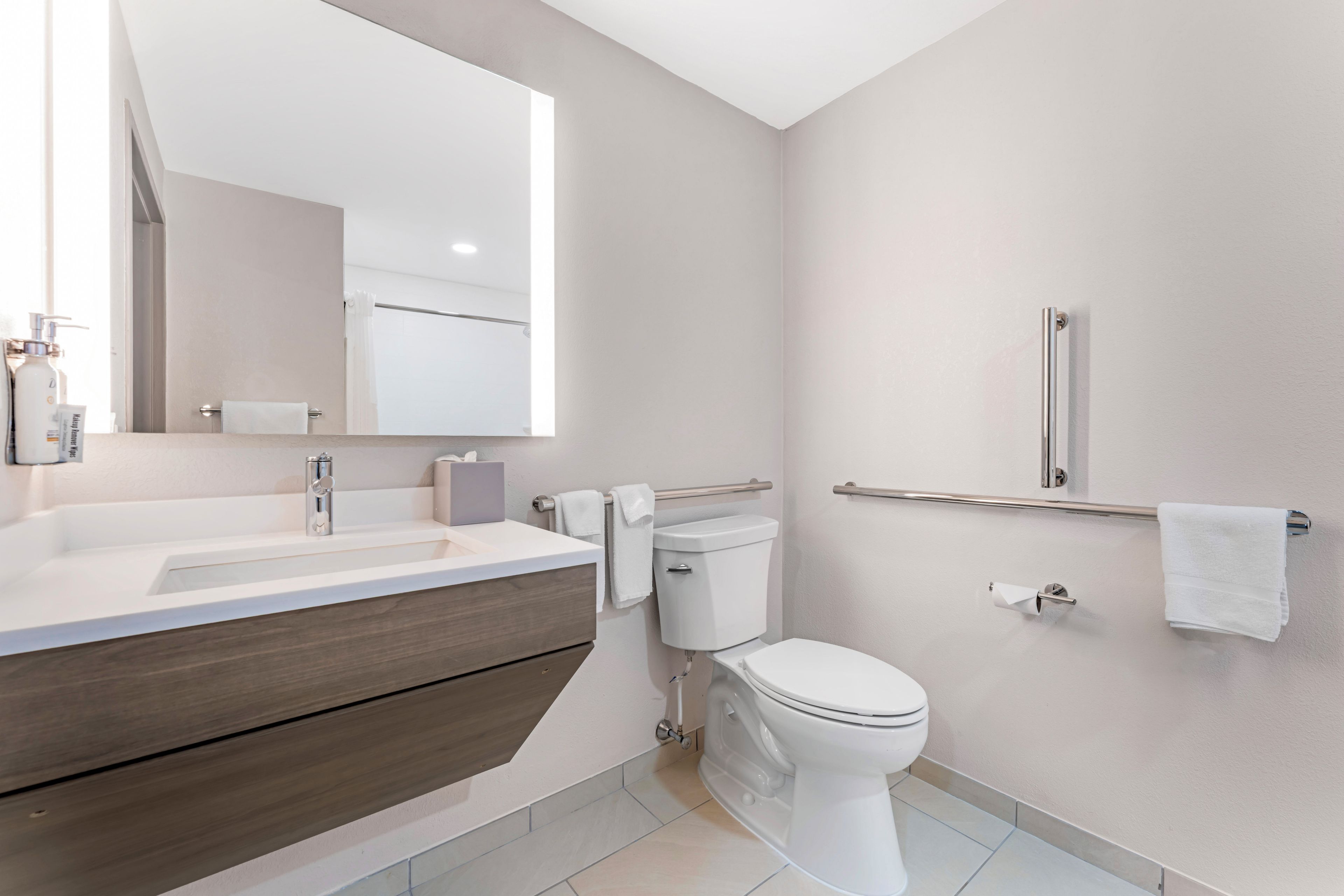 A modern bathroom with a sink, mirror, toilet, and grab bars.