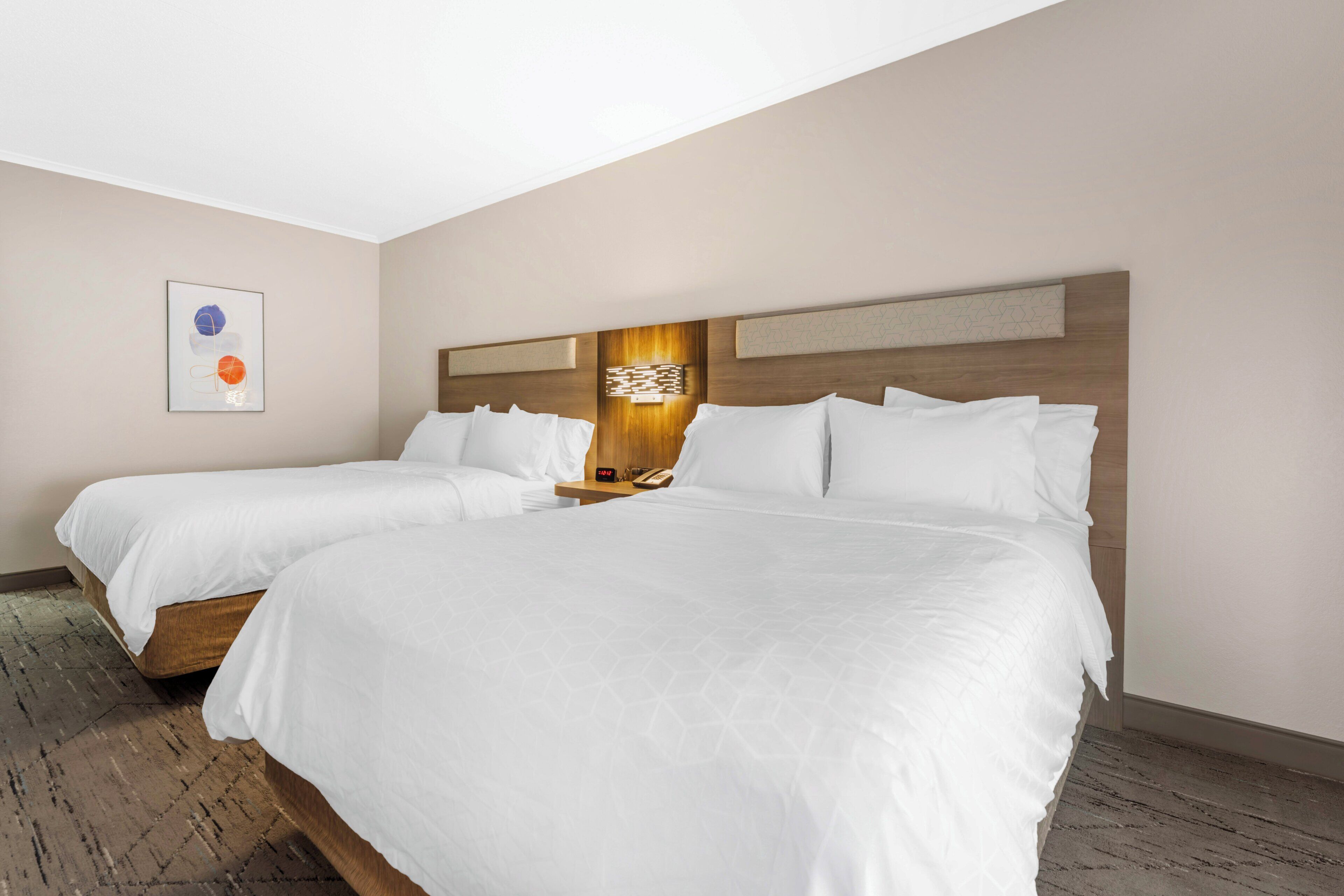 A hotel room with two beds, a nightstand with a phone, and a wall-mounted light fixture.