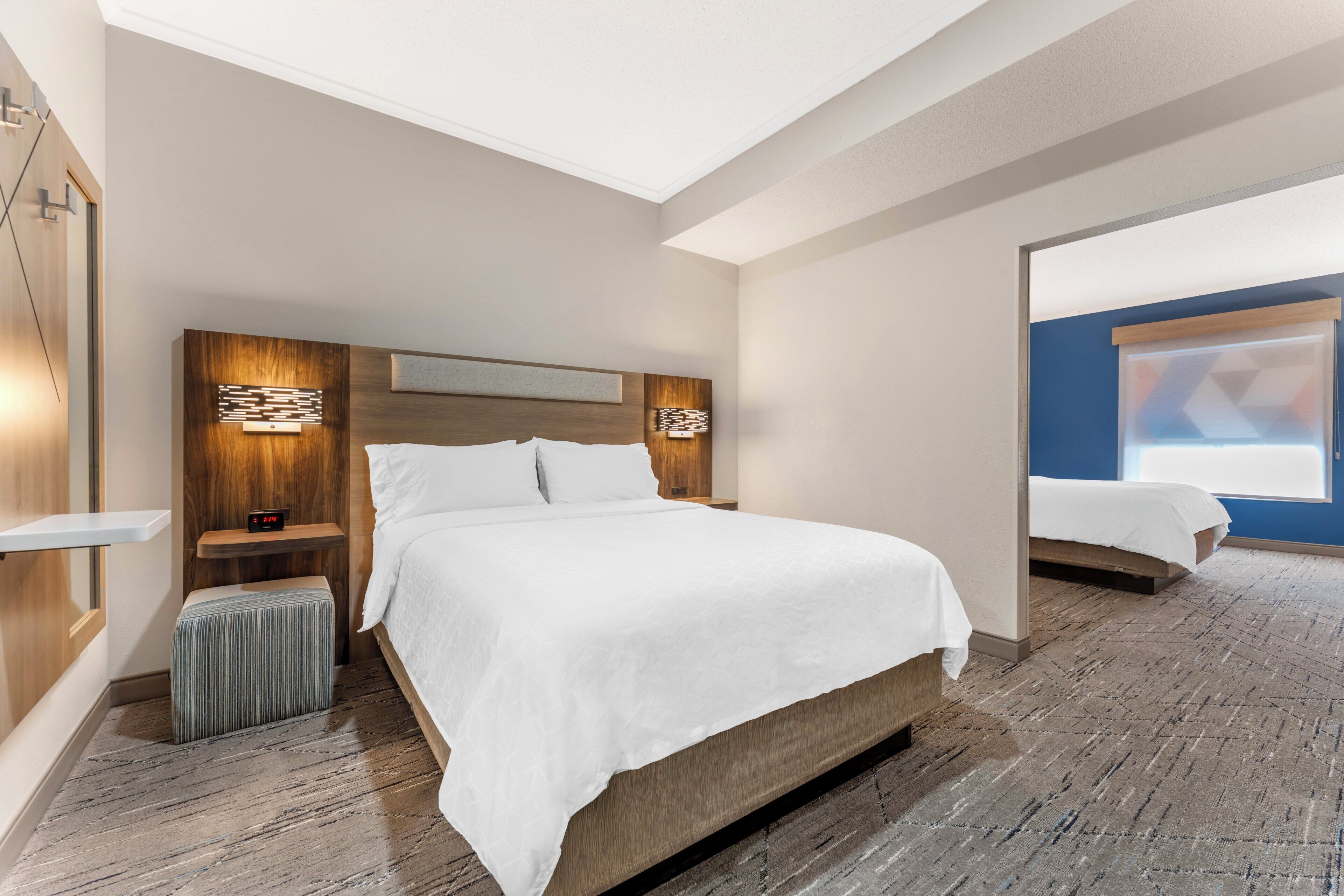A hotel room with a large bed, bedside tables, a nightstand, a wall-mounted clock, and a mirror.