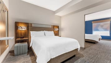 A hotel room with a large bed, bedside tables, a nightstand, a wall-mounted clock, and a mirror.