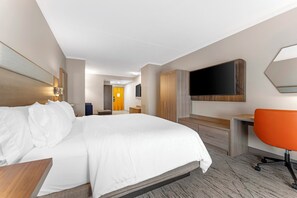 Ein Hotelzimmer mit einem großen Bett, einem Schreibtisch, einem Sessel und einem an der Wand befestigten Fernseher.