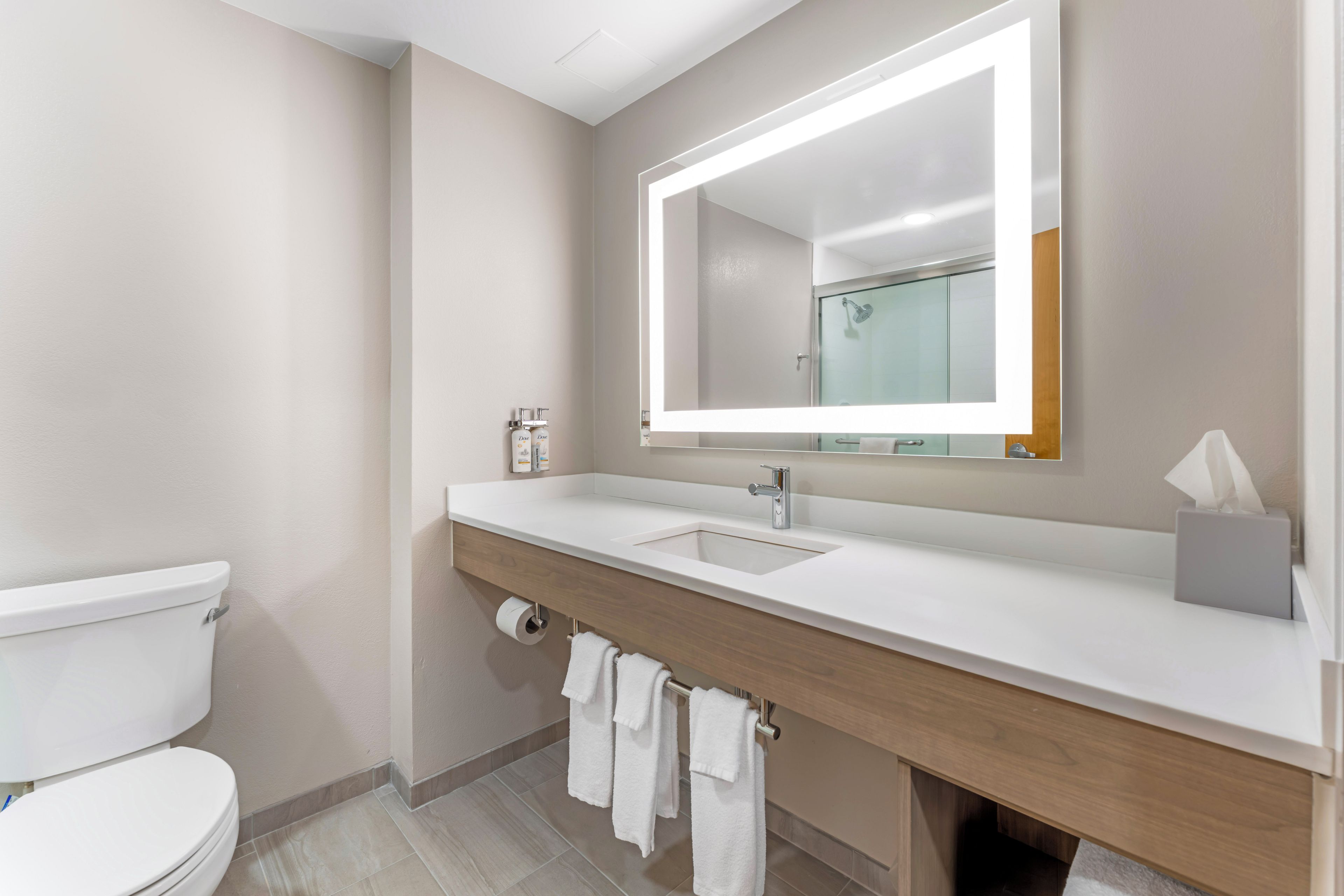 A modern bathroom with a white toilet, a sink, and a mirror with built-in lighting.