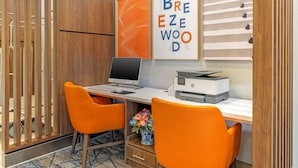 A modern office space with a desk, two orange chairs, a laptop, a printer, and decorative wall art. - Holiday Inn Express Breezewood by IHG (Breezewood)