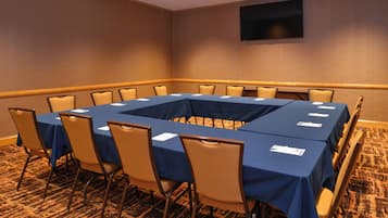 Une salle de conférence avec une table rectangulaire entourée de chaises, un téléviseur à écran plat fixé au mur et un revêtement de sol en moquette.