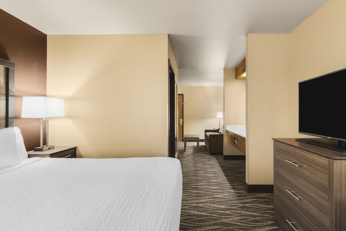 A hotel room with a large bed, a flat-screen TV, a dresser, and a desk with a chair.