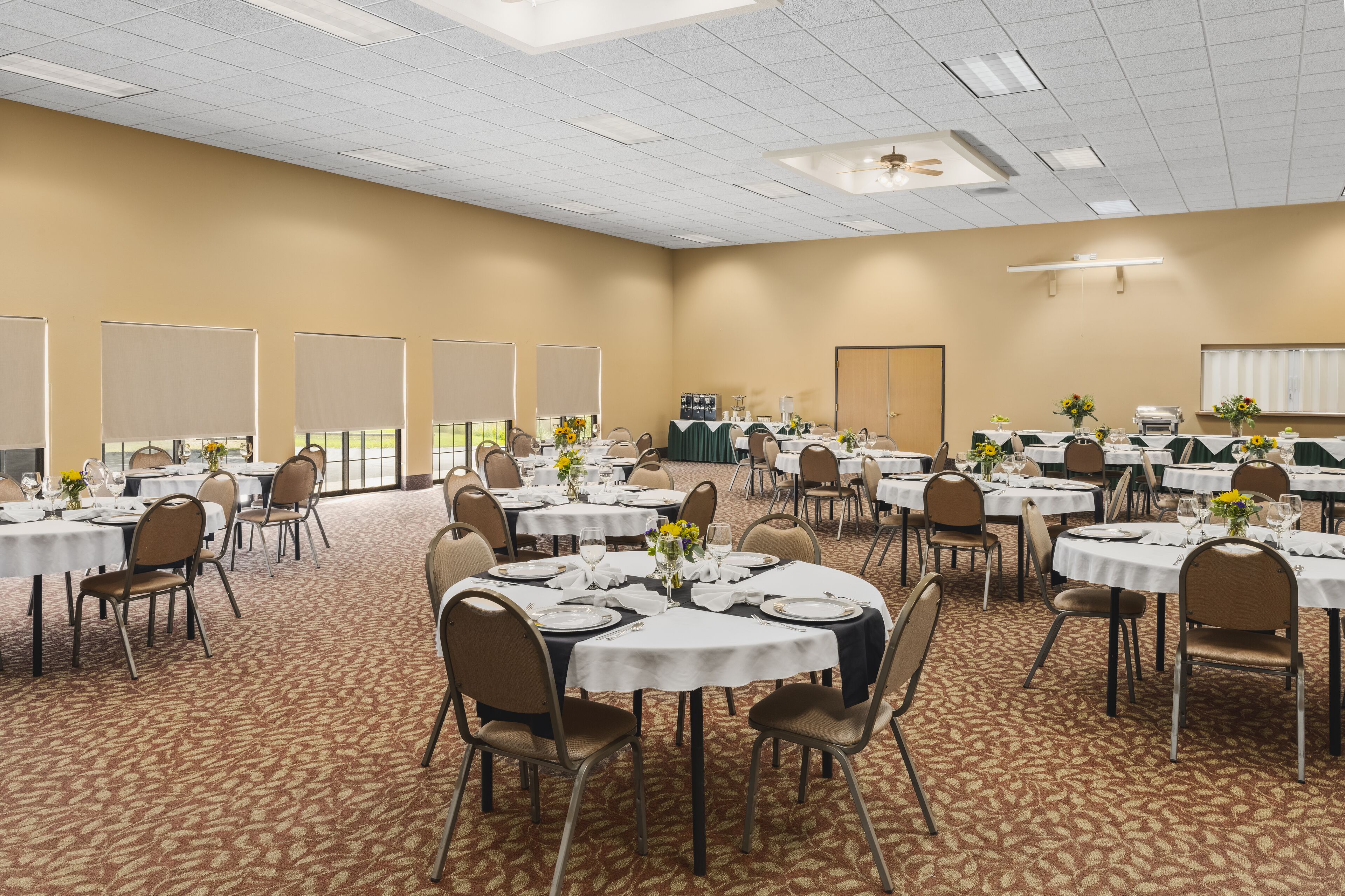 Un amplio salón de conferencias con varias mesas redondas, cada una con mantel blanco, sillas y centros de mesa florales.