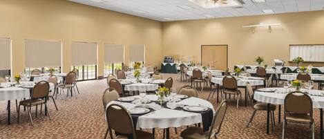 Un amplio salón de conferencias con varias mesas redondas, cada una con mantel blanco, sillas y centros de mesa florales.