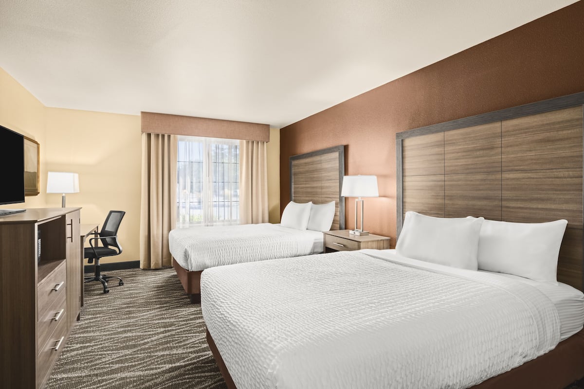 A hotel room with two beds, a desk, a chair, a TV, and a window with curtains.