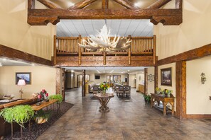 A spacious lobby with a high ceiling, wooden beams, a chandelier, a central table with flowers, and a seating area with a sofa and chairs. - Bitterroot River Inn & Conference Center (Hamilton)
