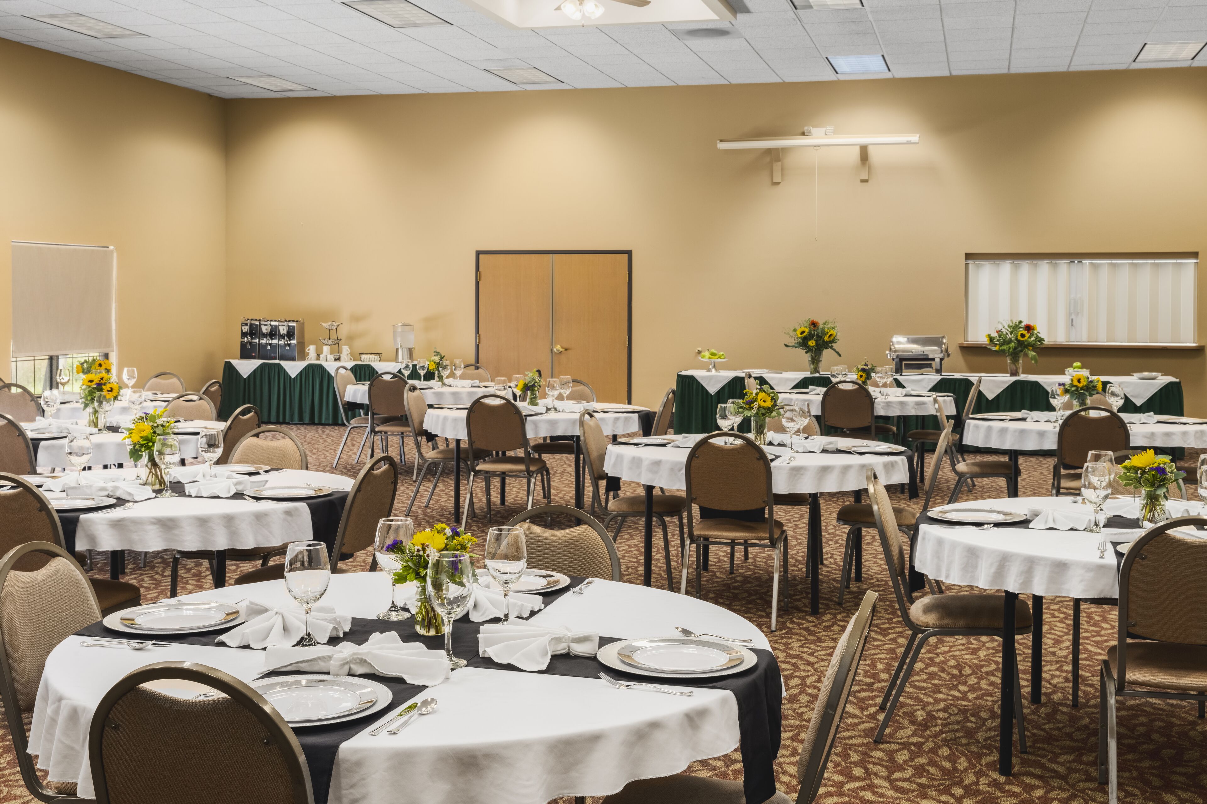 A conference room with multiple tables set for dining, each with white tablecloths and floral centerpieces.