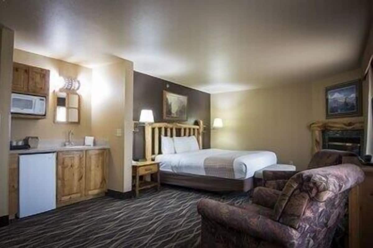 A hotel room with a bed, a chair, a desk, a microwave, and a refrigerator.