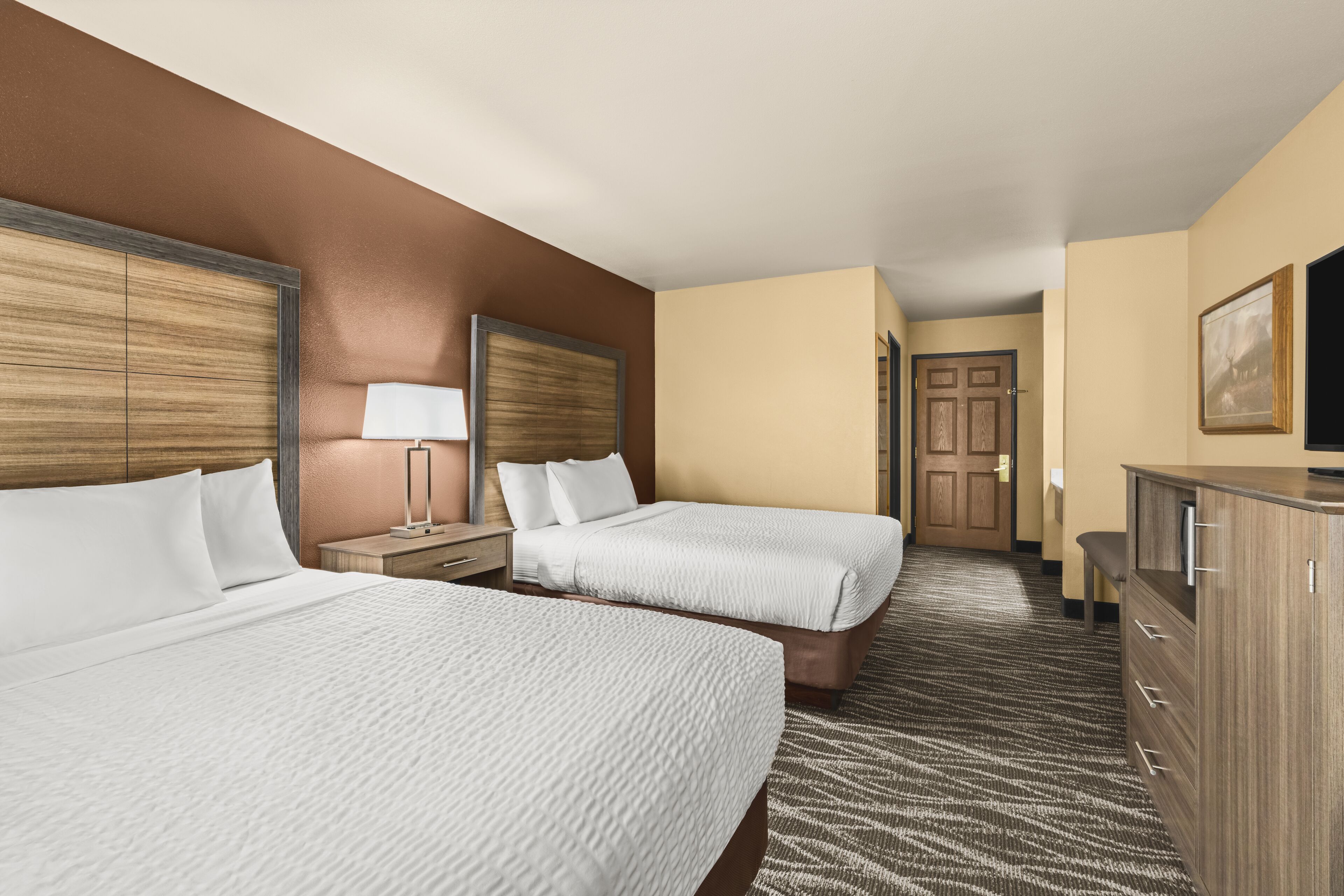A hotel room with two beds, a desk, a dresser, and a television.