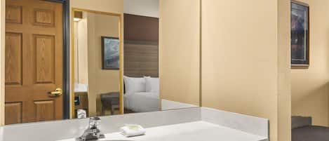 A bathroom with a large mirror, a sink, and a door leading to a bedroom.