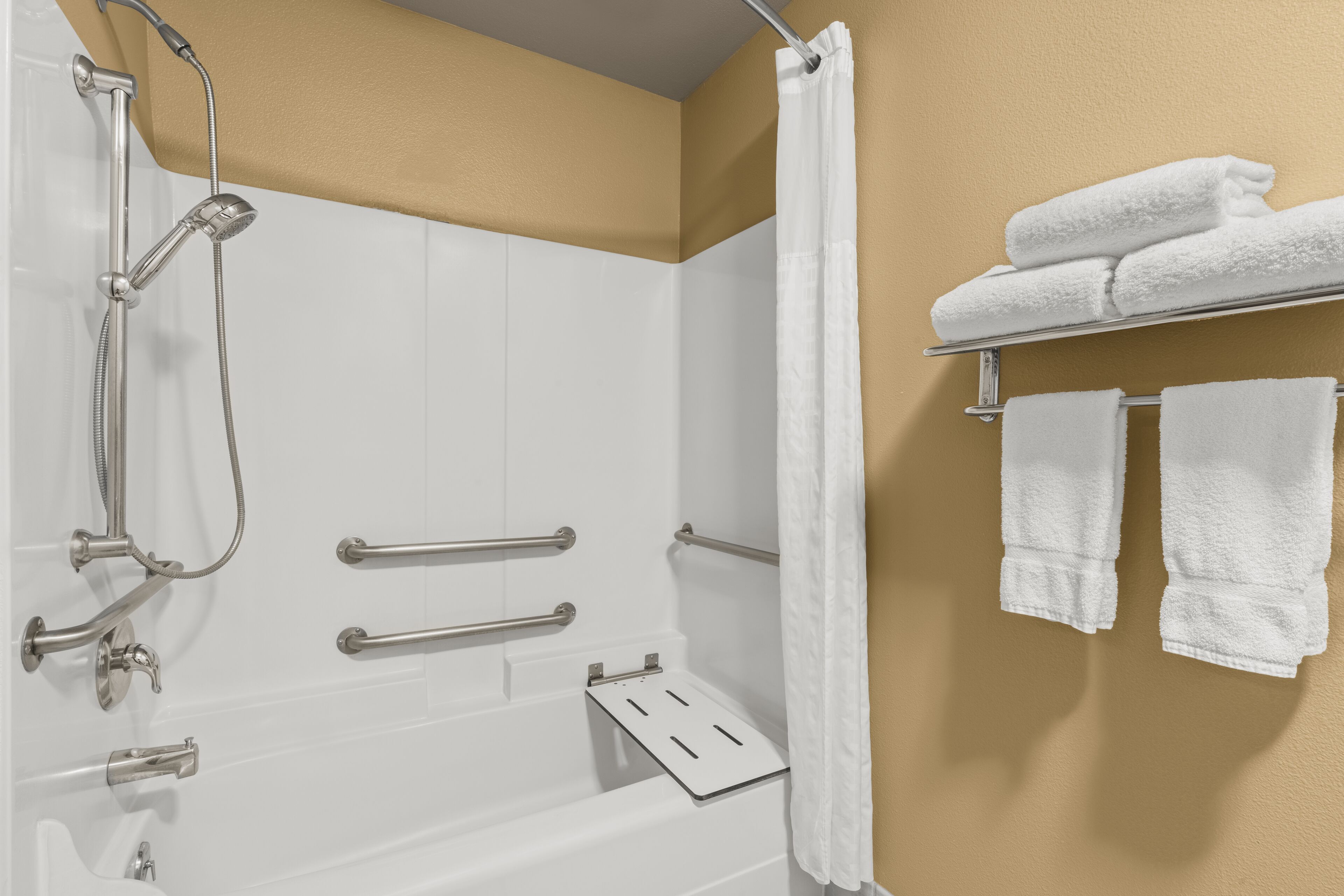 A bathroom with a bathtub, shower, grab bars, a towel rack with towels, and a shower curtain.