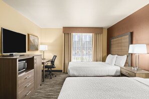 A hotel room with a large bed, a desk with a chair, a television, and a window with curtains.