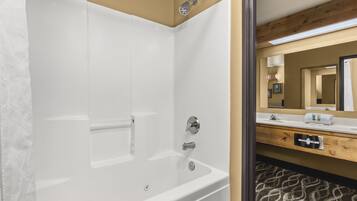 Un baño moderno con una bañera blanca, un tocador de madera con espejo y una alfombra estampada en el suelo.