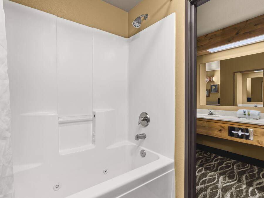 Un baño moderno con una bañera blanca, un tocador de madera con espejo y una alfombra estampada en el suelo.