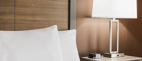 A hotel room with a wooden headboard, a bedside table with a lamp, and a drawer.