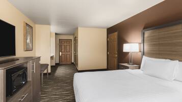 A hotel room with a bed, a television on a cabinet, a desk with a lamp, and a door leading to another room.