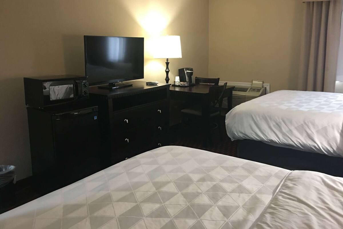 A hotel room with two beds, a television, a desk with a lamp, and a minibar.