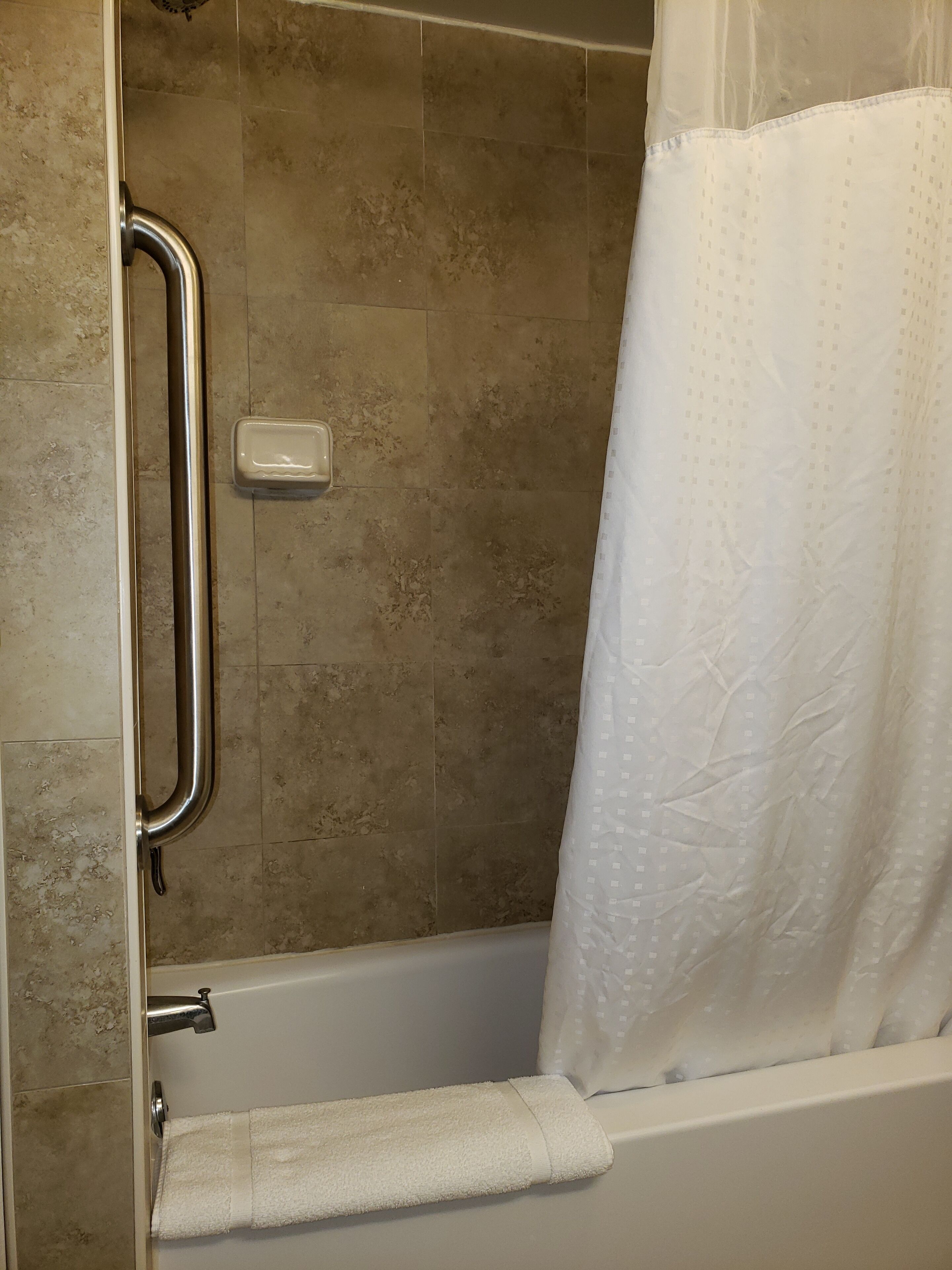 A bathroom with a shower, a handrail, a soap dish, and a towel rack.