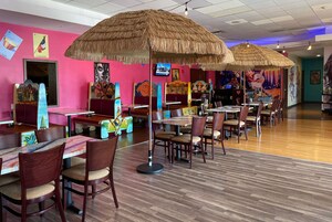 Un restaurante con mesas y sillas de madera, sombrillas de paja y murales coloridos en las paredes.