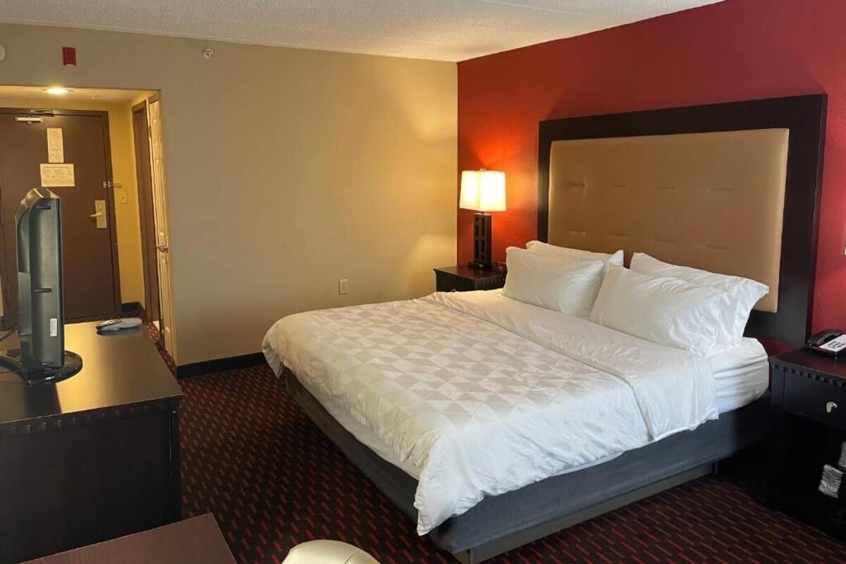 A hotel room with a large bed, a desk with a lamp, and a door leading to the bathroom.