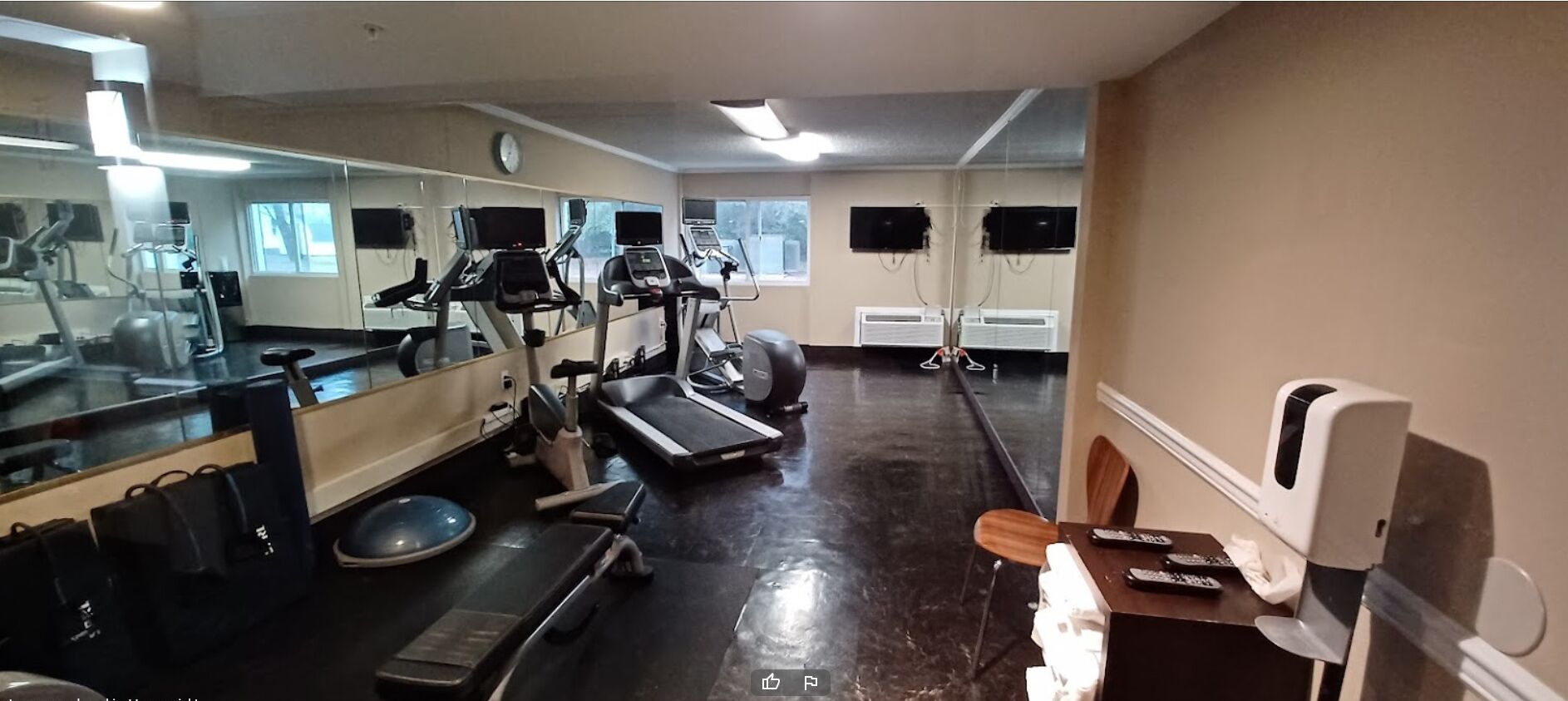 A gym with exercise equipment, a mirror, a clock, and a TV on the wall.