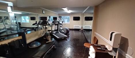 Un gimnasio con equipo de ejercicio, un espejo, un reloj y un televisor en la pared.