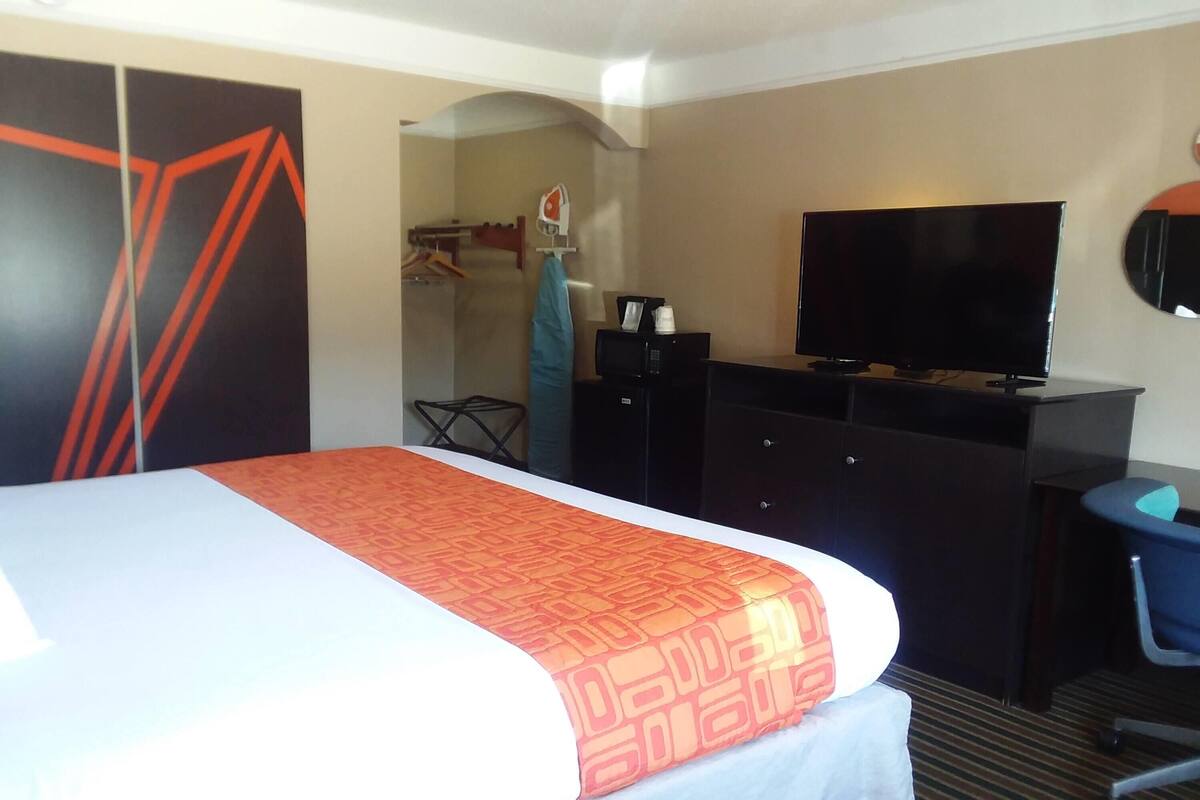 Ein Hotelzimmer mit Bett, Fernseher, Schreibtisch und Kleiderschrank.