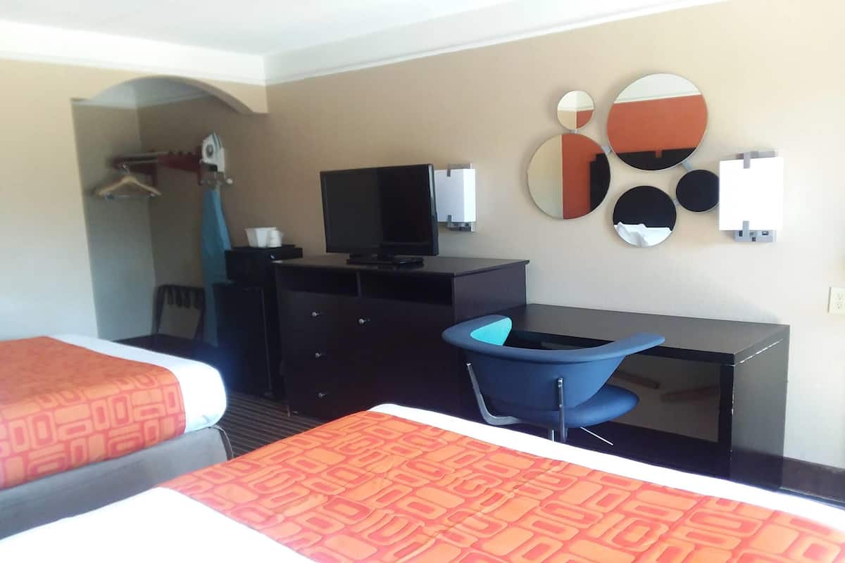 Ein Hotelzimmer mit zwei Betten, einem Schreibtisch mit Computer, einem Sessel, einem Fernseher und einer Wand mit Spiegeln.