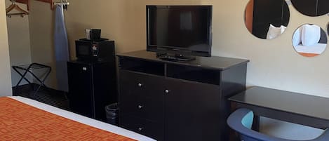 Una habitación de hotel con cama, escritorio con televisor, silla y perchero.