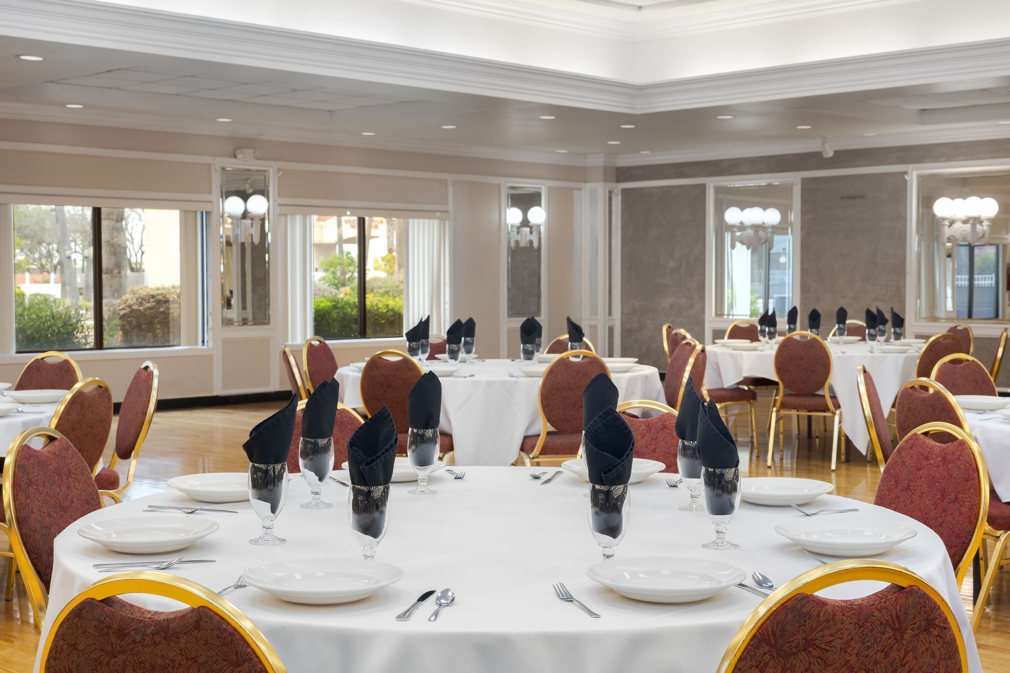 A banquet hall with round tables, red upholstered chairs, and white tablecloths.