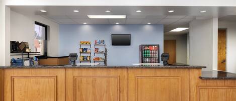 A reception area with a wooden counter, a flat-screen TV mounted on the wall, and a window with a view of palm trees.