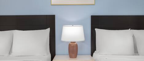 Ein Hotelzimmer mit zwei Betten, einem Nachttisch mit Lampe, einem gerahmten Bild an der Wand und einer hellblauen Wand.