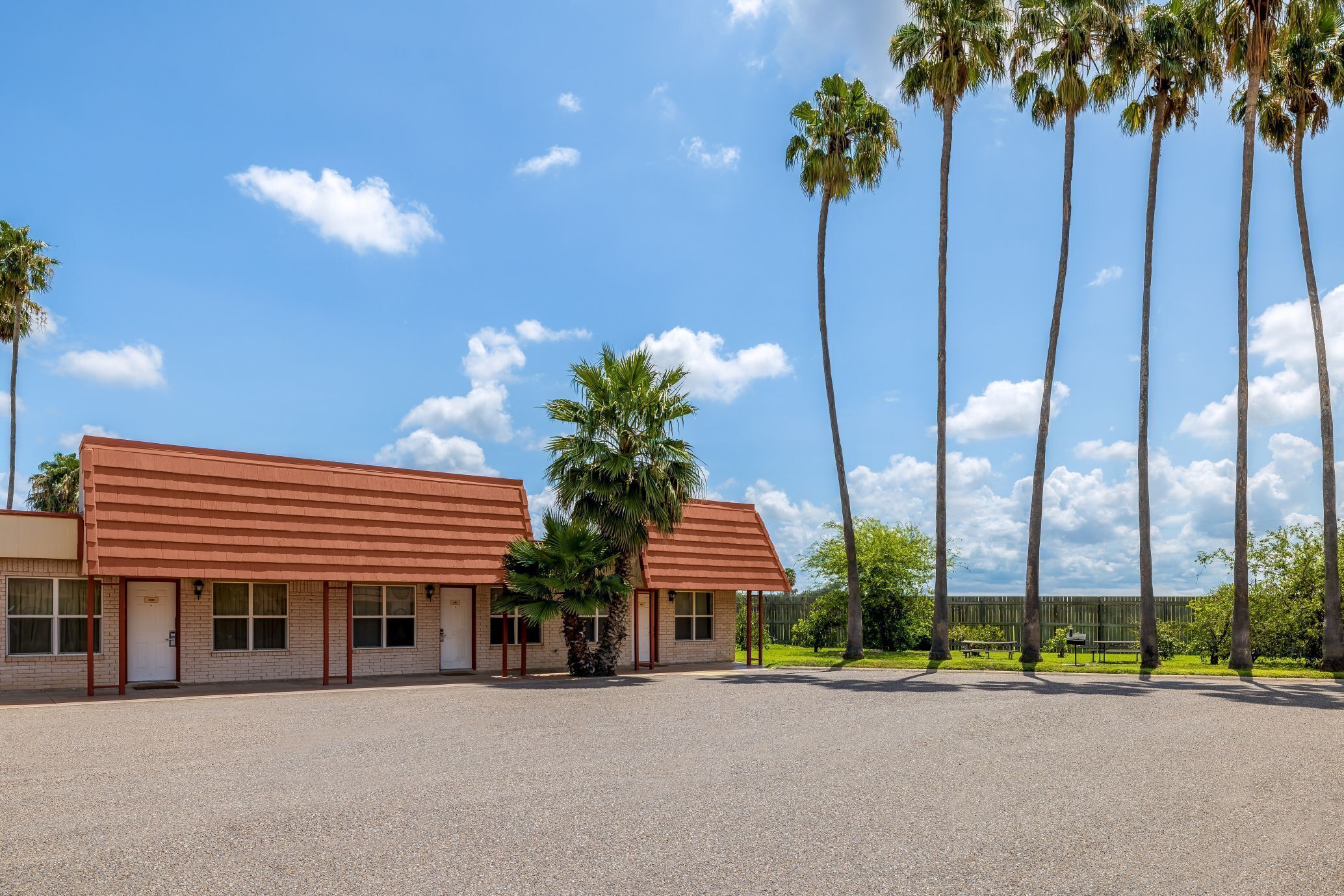 Ein Motel mit zweistöckigen Gebäuden, einem Kiesparkplatz und hohen Palmen.