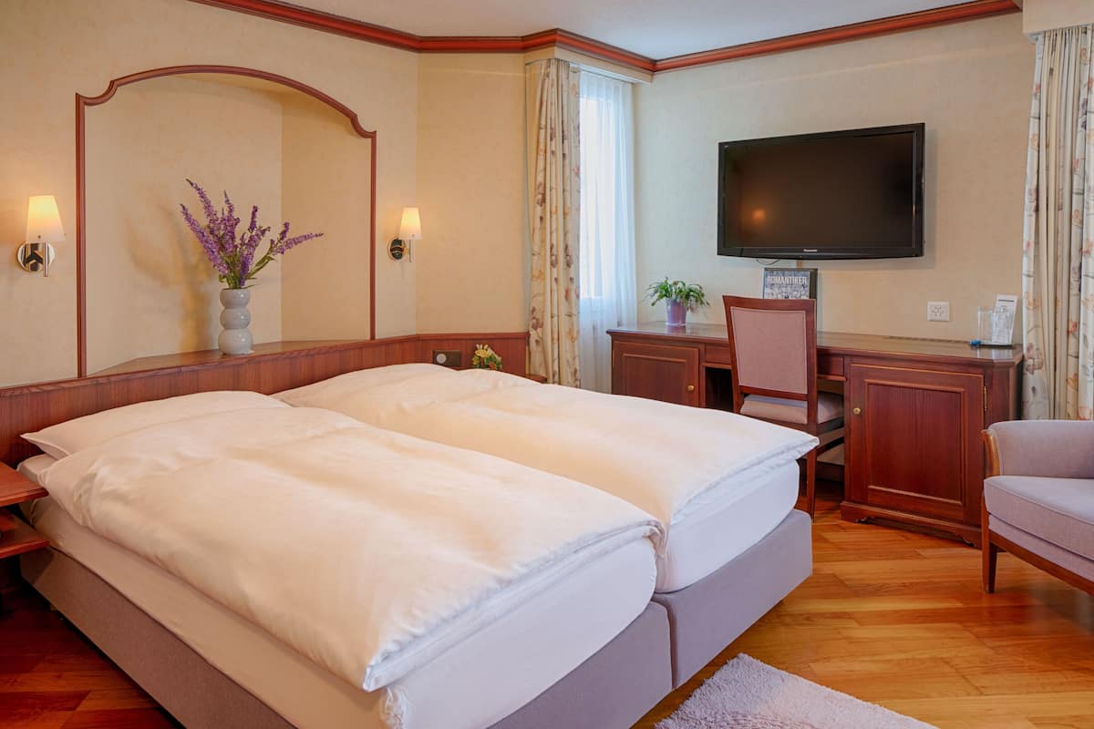 Habitación de hotel con cama doble, escritorio con silla, televisión y un florero con flores.