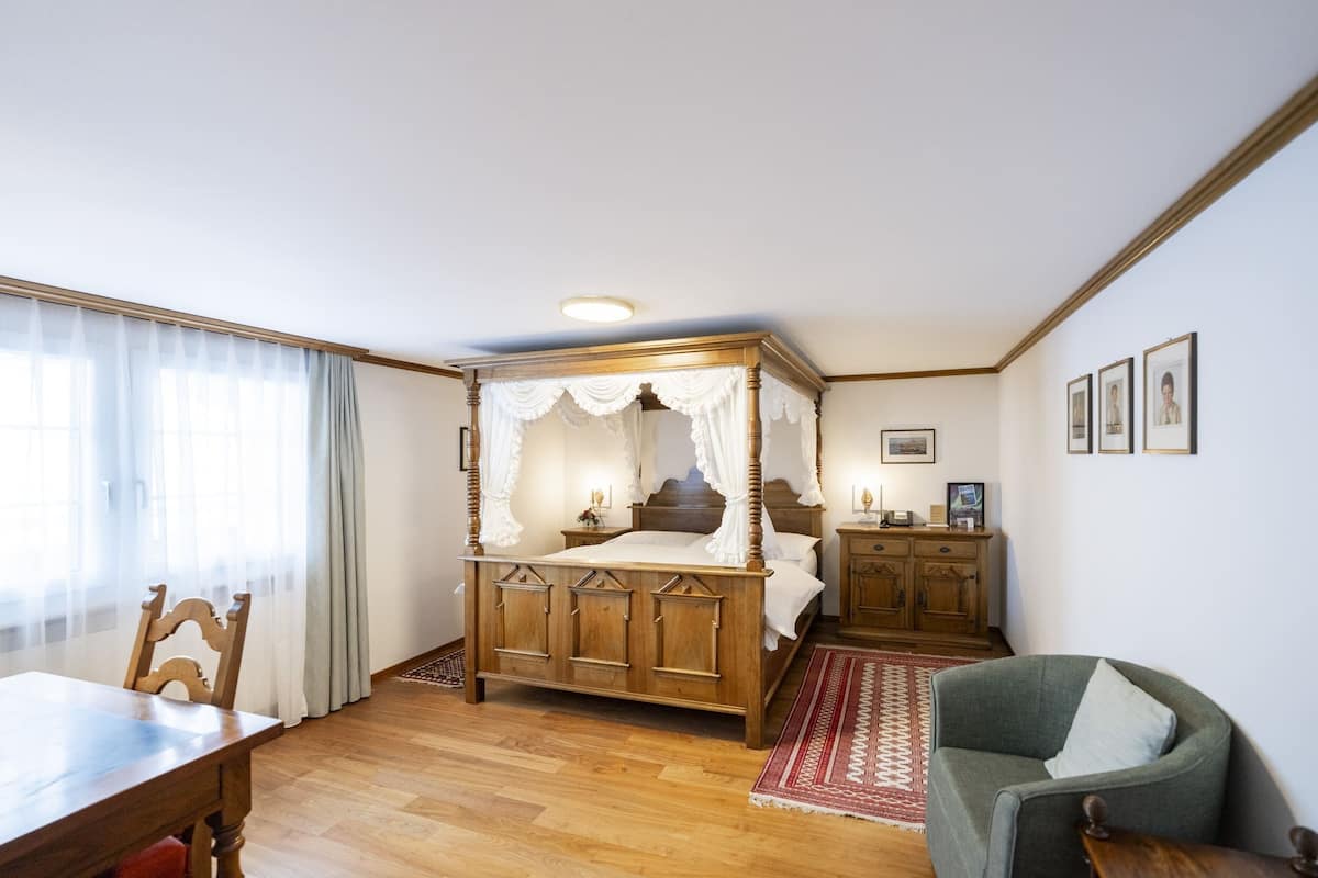 Un dormitorio con cama de dos columnas, muebles de madera, una mesa de comedor y una silla.