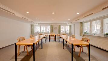 A conference room with a long table and chairs, large windows with curtains, and a carpeted floor.