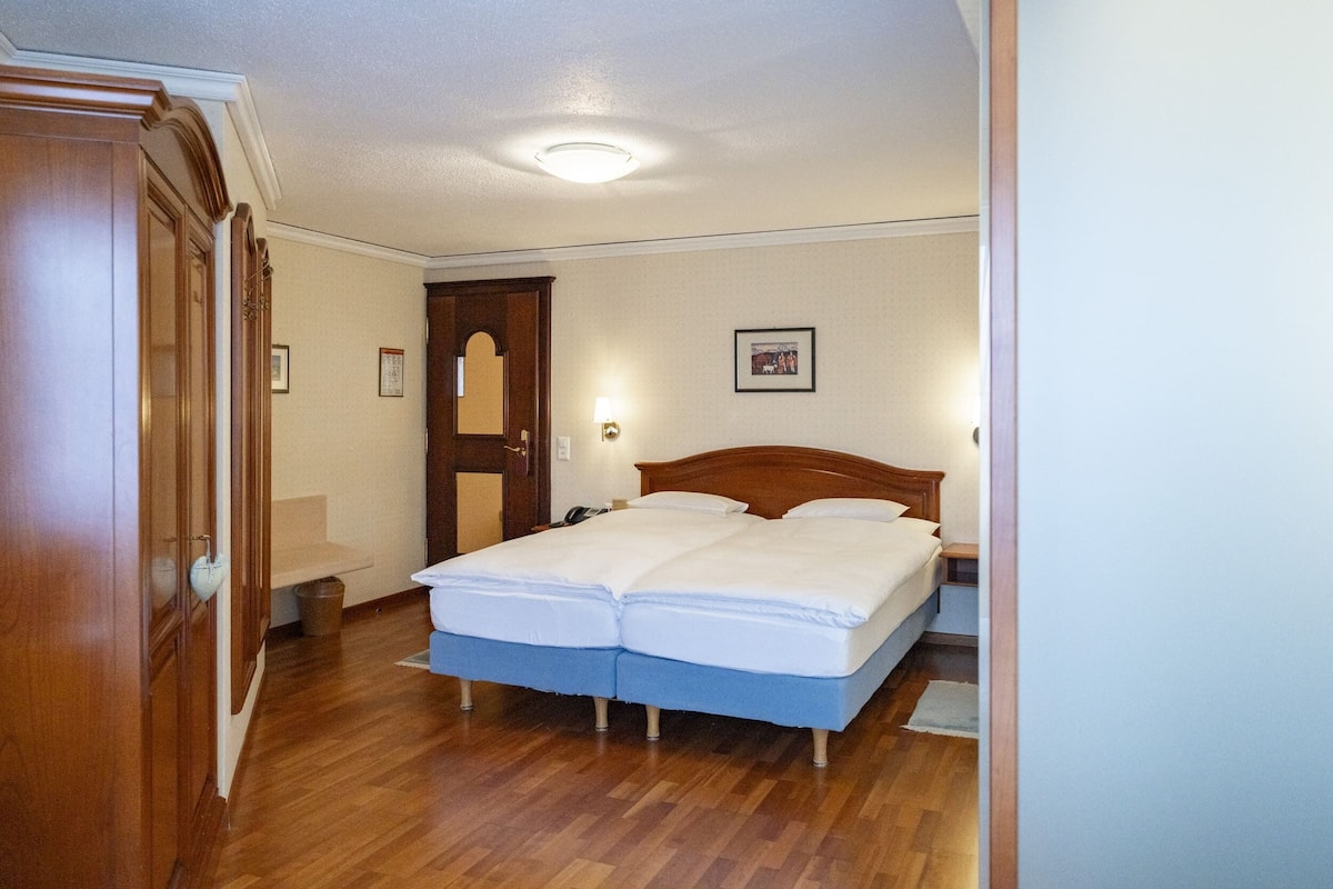 Un dormitorio con cama doble, armario de madera y una mesita de noche pequeña.