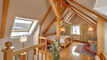 Un dormitorio acogedor en el ático, con techo inclinado, vigas de madera, cama, escritorio y ventana con cortinas.