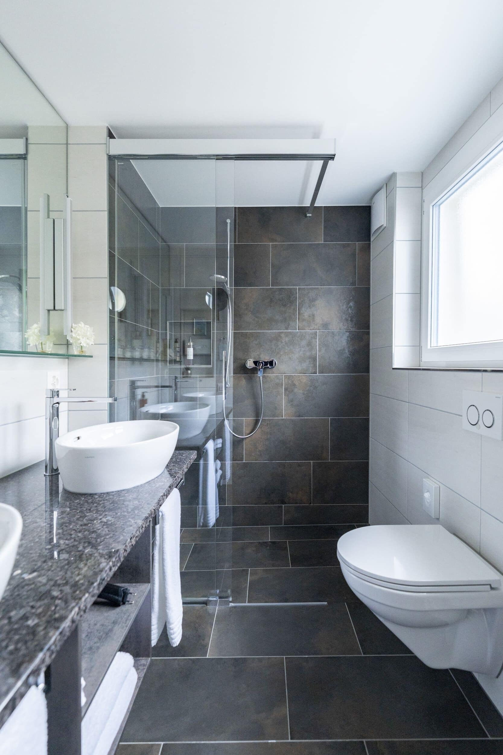 Een moderne badkamer met twee wastafels, een douche en een toilet.
