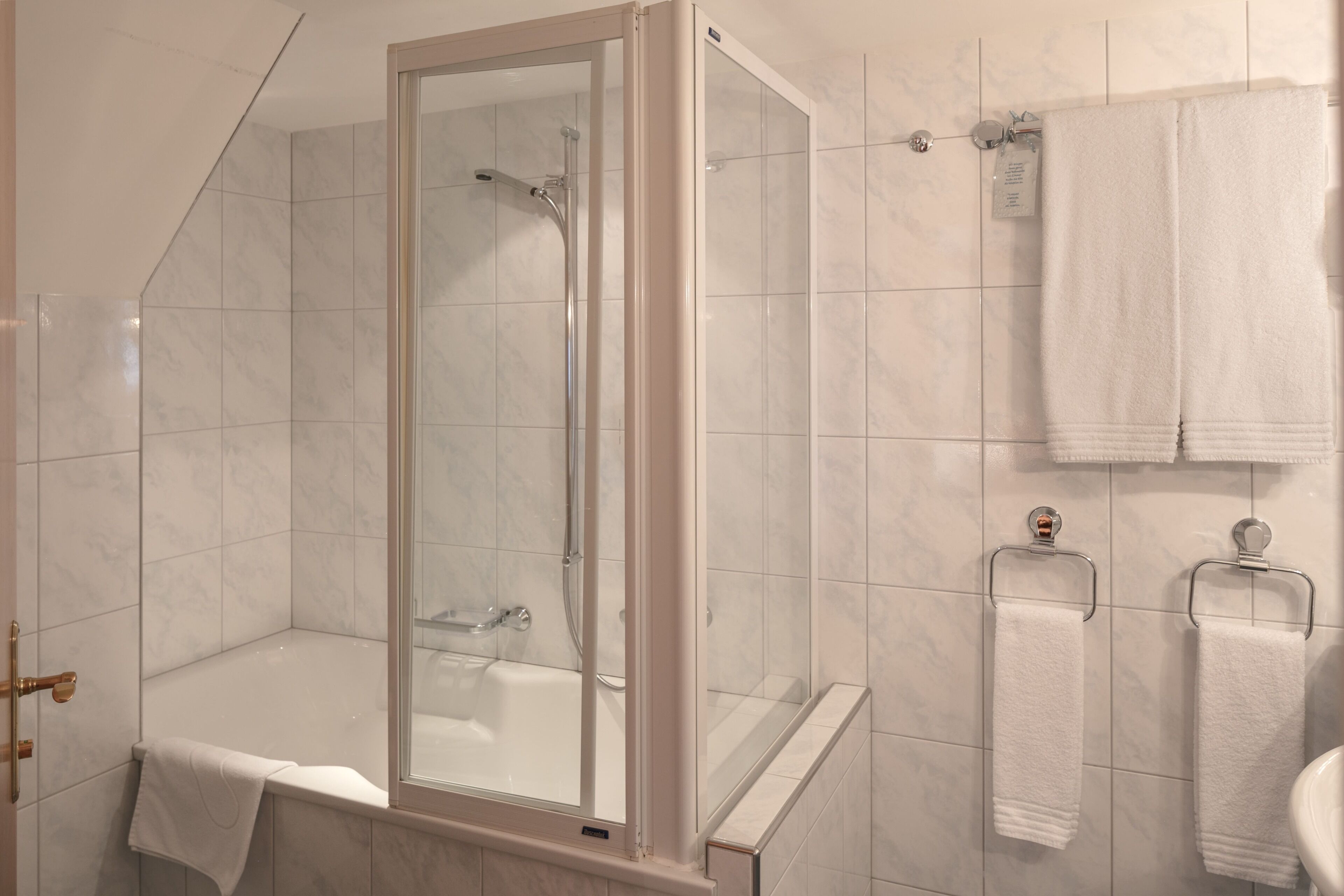 Ein modernes Badezimmer mit einer gläsernen Duschkabine, einer Badewanne und zwei Handtuchhaltern mit weißen Handtüchern.