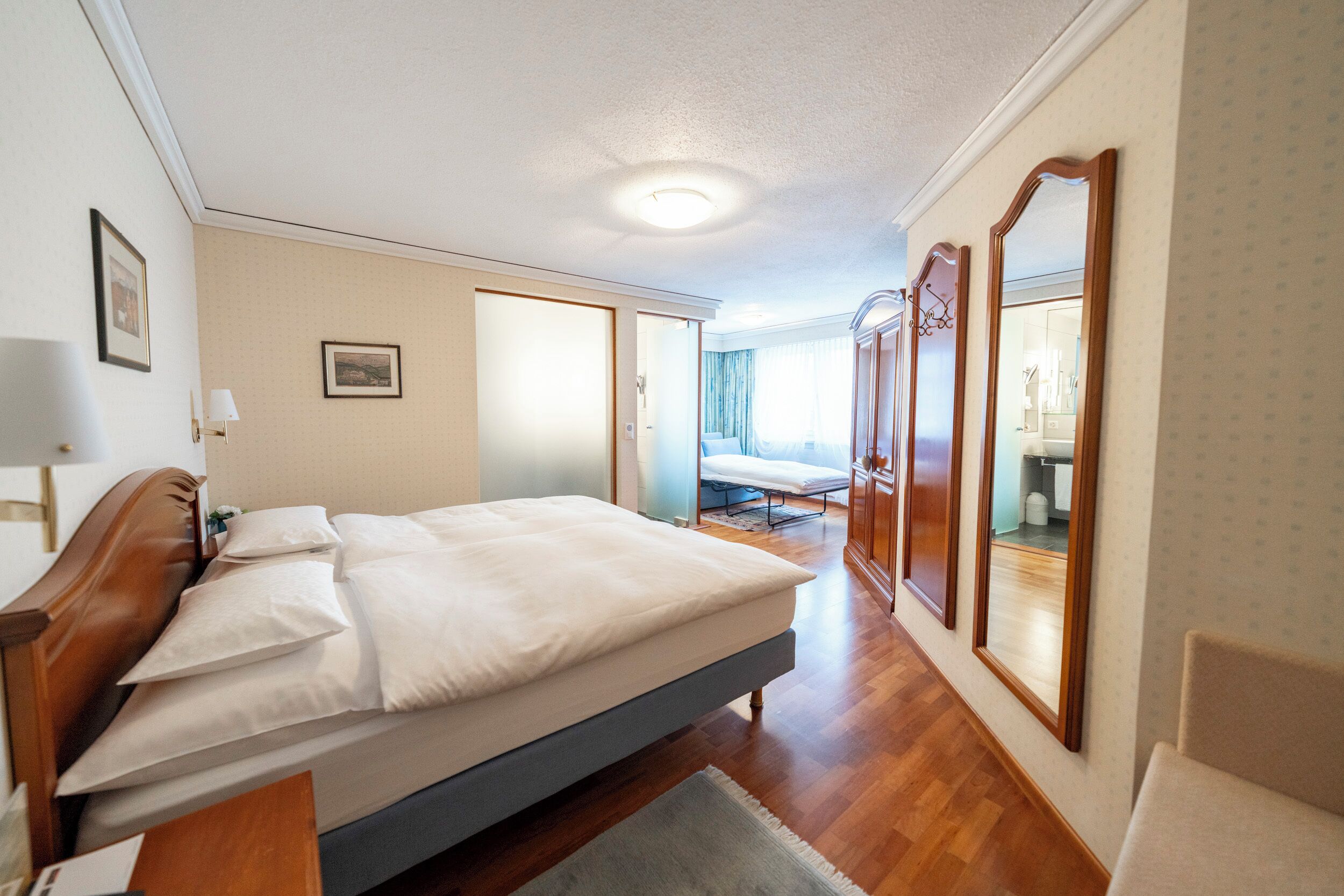 A hotel room with a bed, a desk, a chair, and a large mirror.