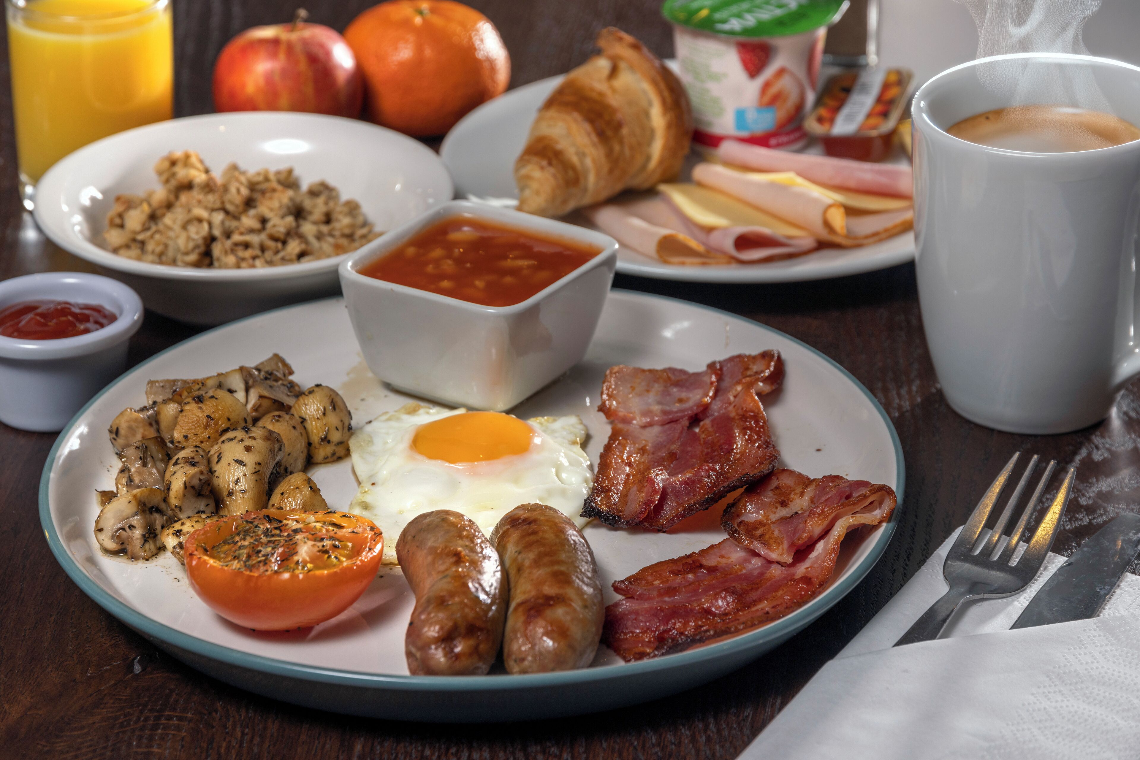A breakfast plate with eggs, bacon, sausages, mushrooms, and a tomato.