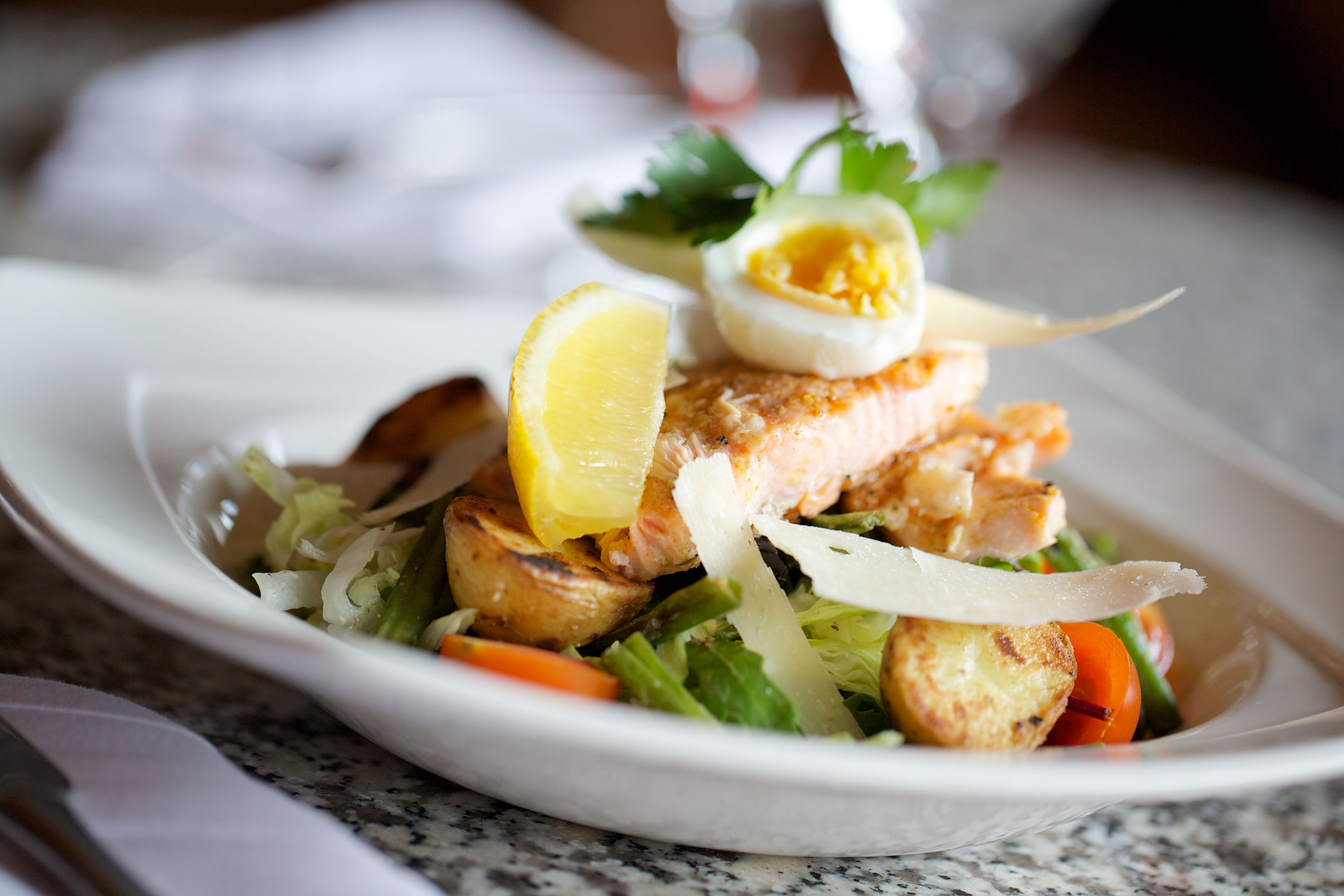 A plate of food with salmon, vegetables, and a lemon slice.